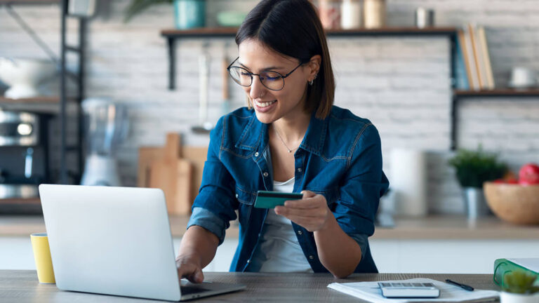 Woman holding business credit card and using laptop.