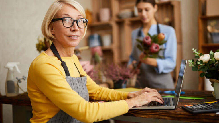 Woman smiling at camera and working on laptop.