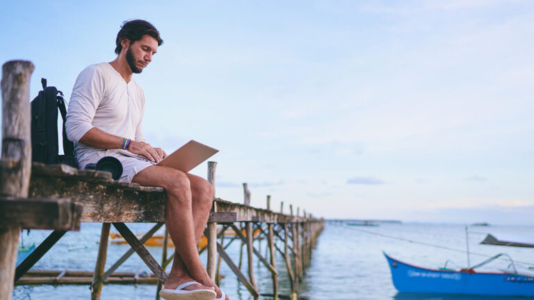 Man sitting on a pier with his laptop.