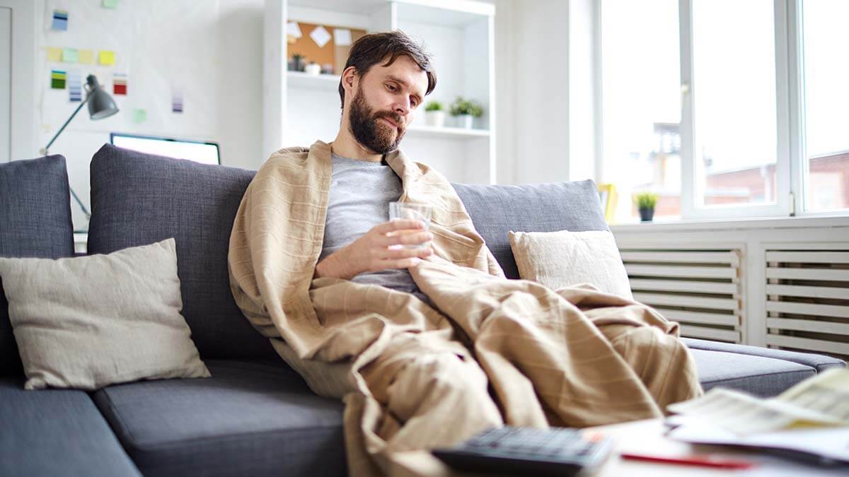 Man in a blanket on the couch, sick.
