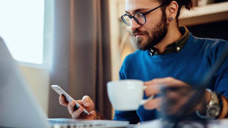Man drinking a cup of tea and looking at phone.