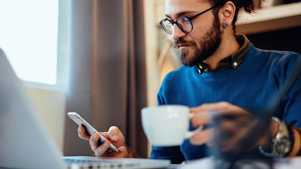 Man drinking a cup of tea and looking at phone.
