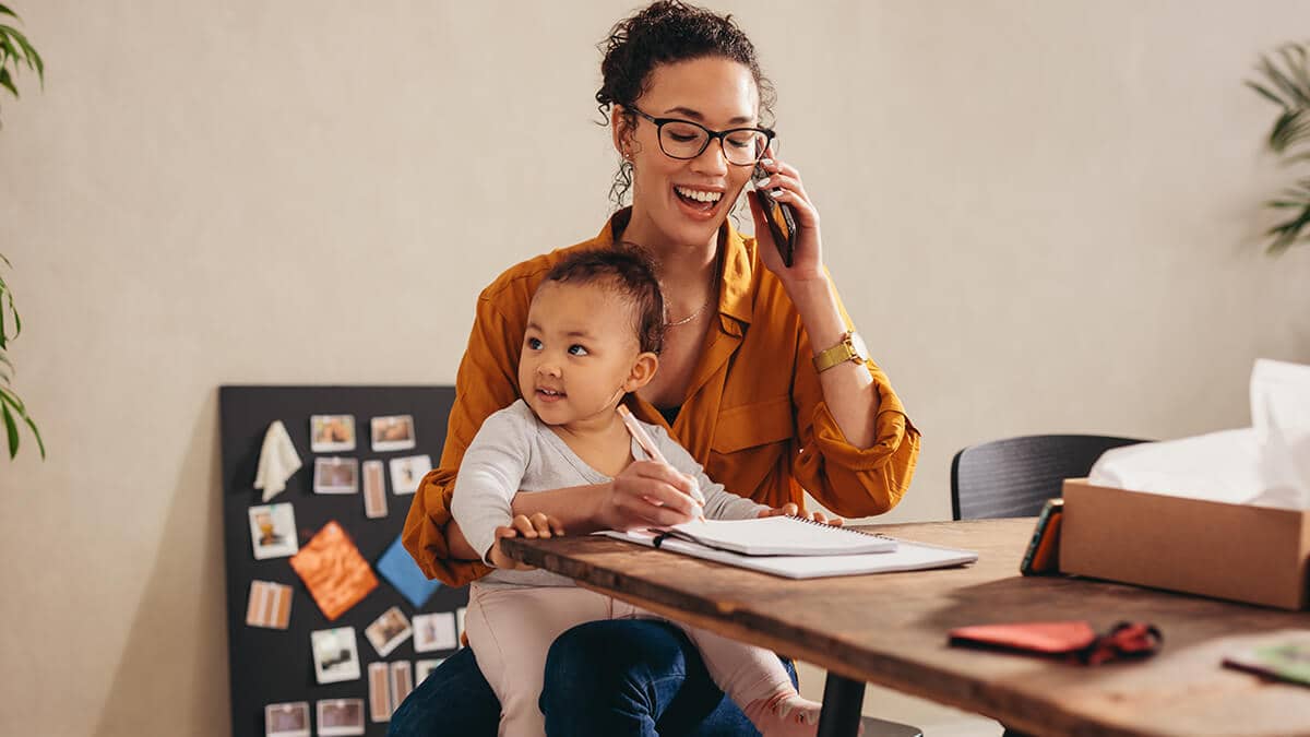 Smiling woman holding her baby while on the phone.
