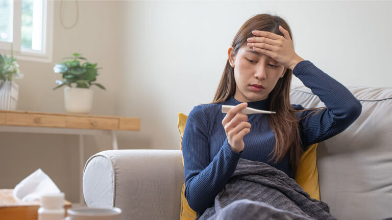 Woman with hand to her head and holding a thermometer, using Colorado paid sick leave.