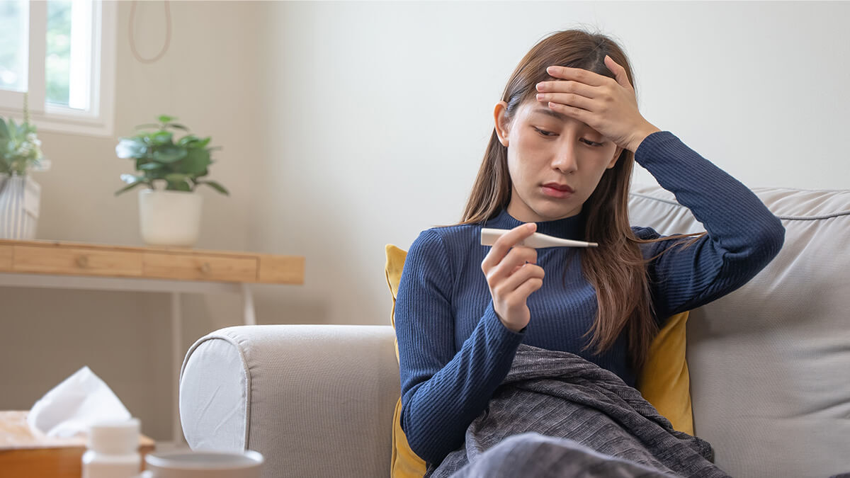 Woman with hand to her head and holding a thermometer, using Colorado paid sick leave.