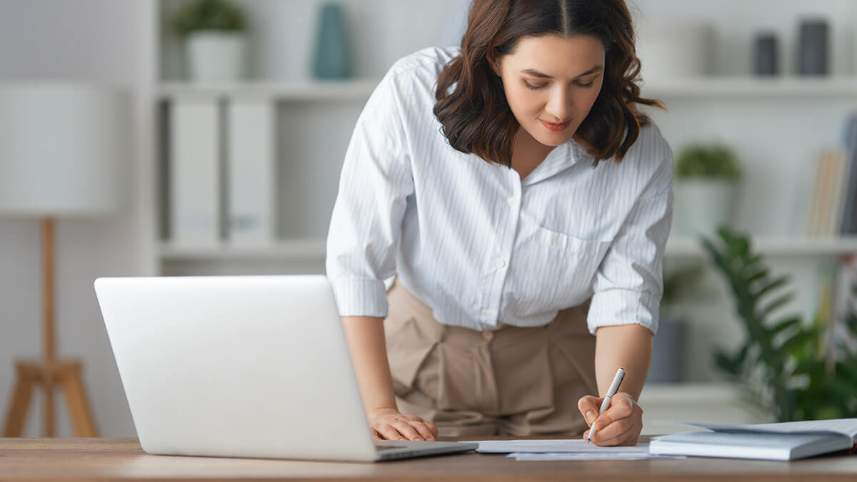 Woman bending down to write on a desk.