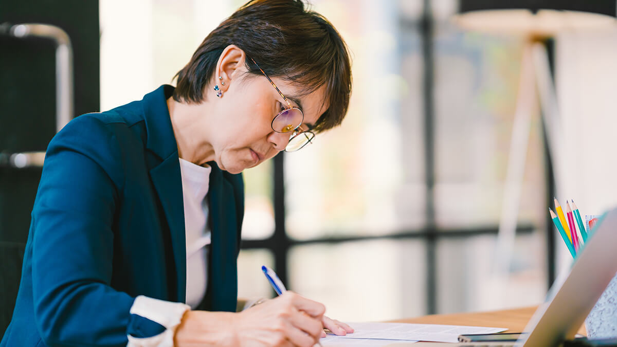 Woman in a blue blazer writing at her desk.