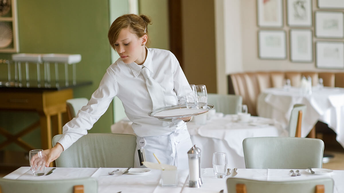 Waitress collecting empty glasses from tables.