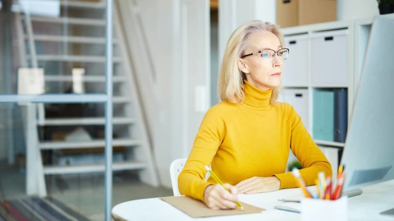 Woman in yellow turtleneck looking at computer.