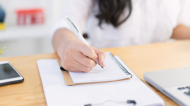 Woman writing in a small notebook.