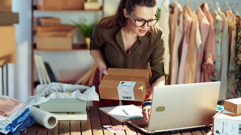 Business owner holding a package and checking her laptop.