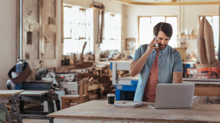 Man on the phone and using a laptop in a work area.