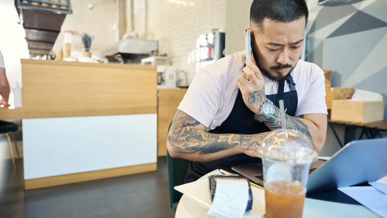 Barista on the phone and working on a laptop.