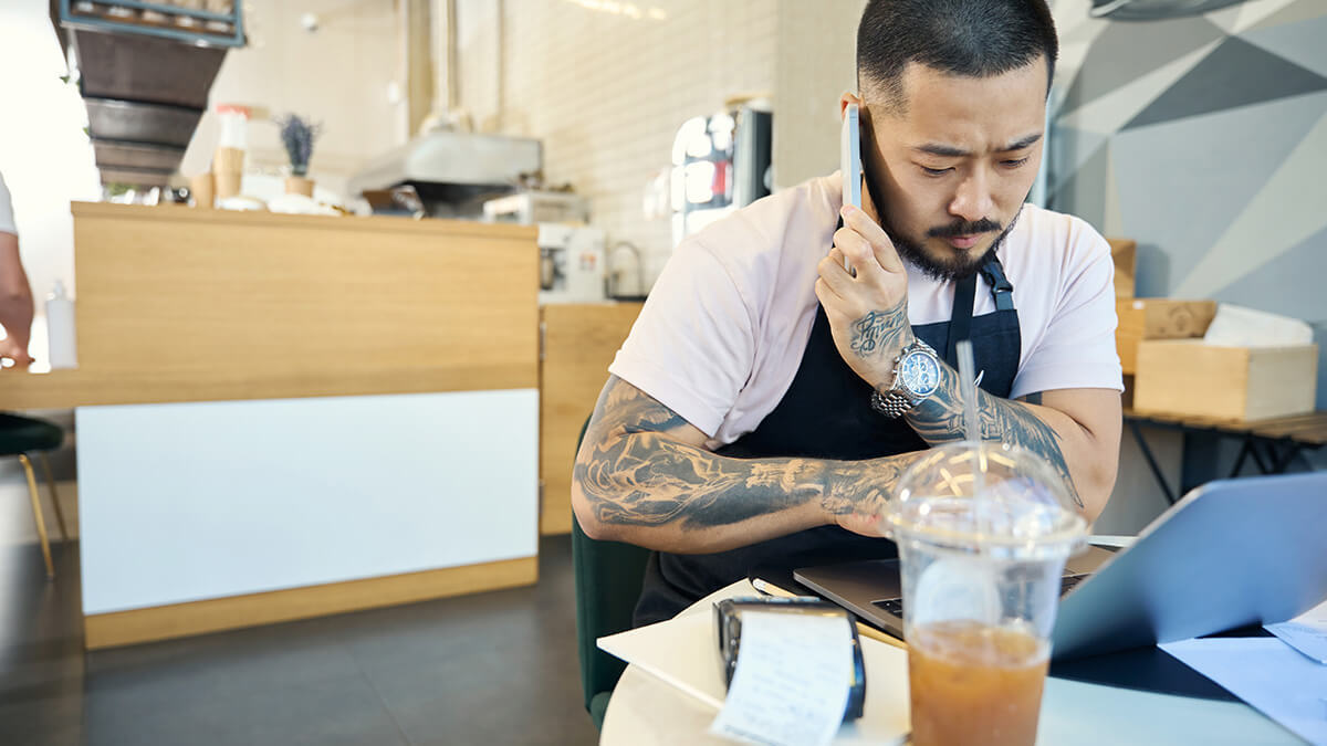 Barista on the phone and working on a laptop.