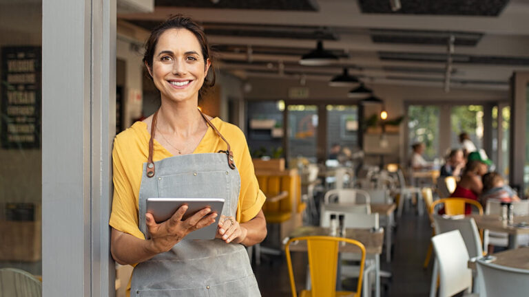Smiling business owner holding tablet in front of restaurant.