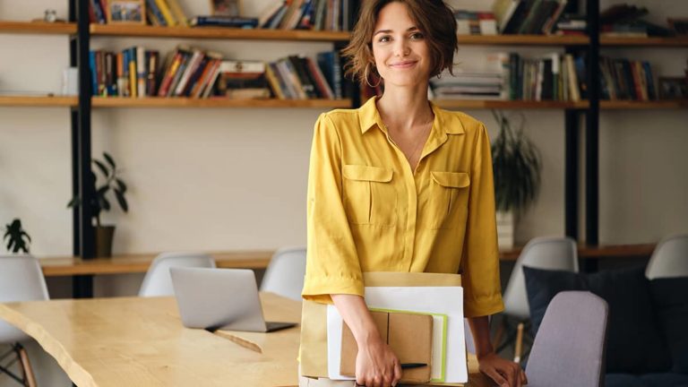 Woman holding papers and smiling slightly at camera.