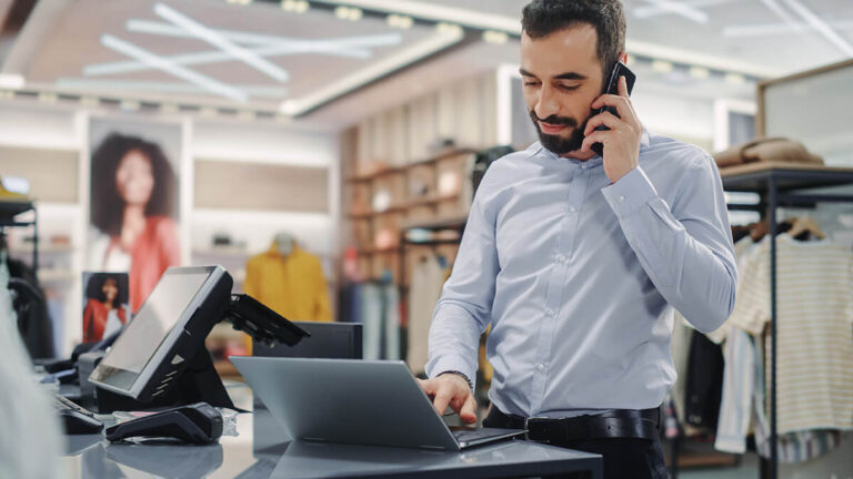 Man on the phone at the counter of a retail store.