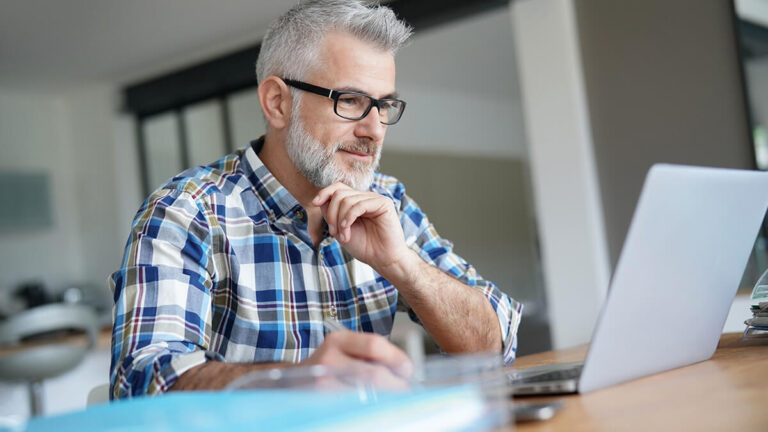 Older man with hand under head looking at a computer.