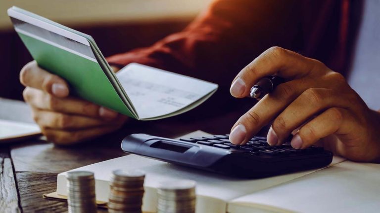 Hands on a calculator and holding a notebook.