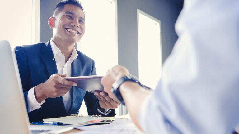 Man handing paperwork to another man.