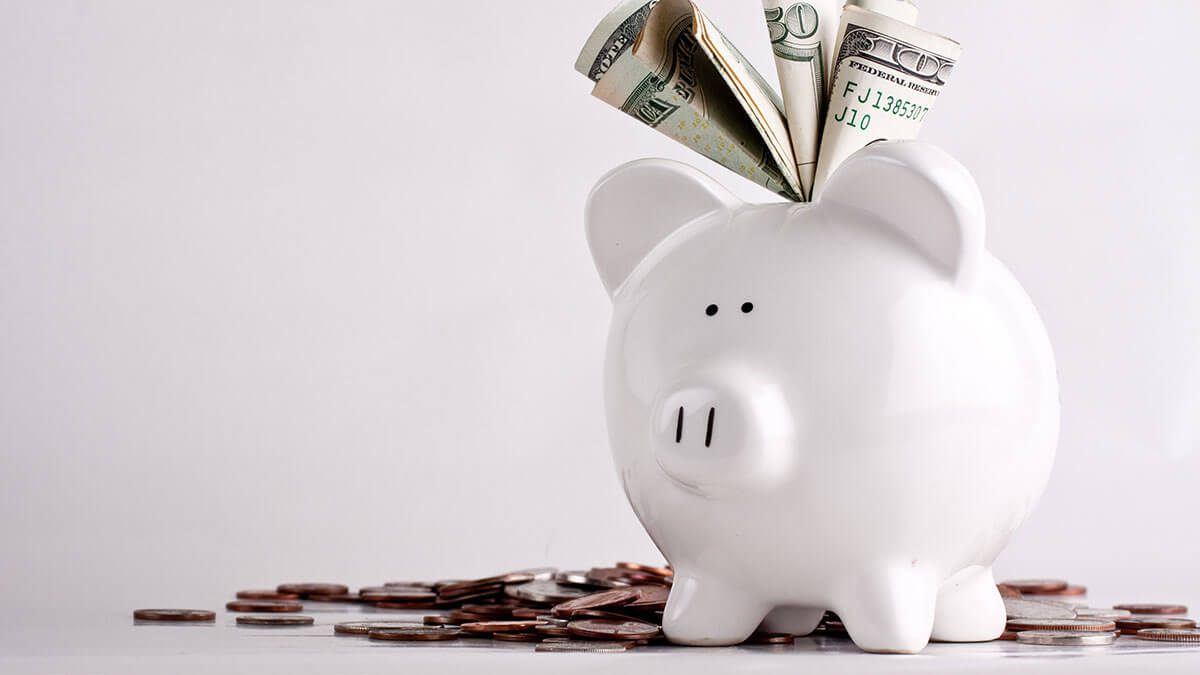 White piggy bank with bills sticking out and coins on the ground.