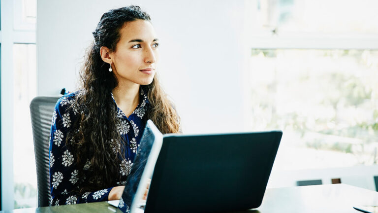 Woman using a laptop and looking off into the distance.