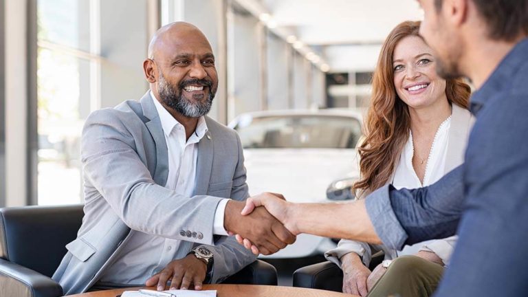 Two men shaking hands next to a smiling woman.