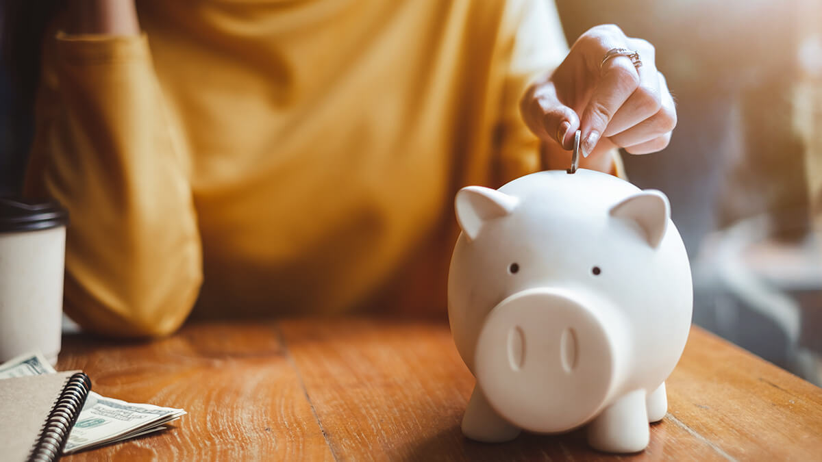 Woman putting a coin into a white piggy bank.