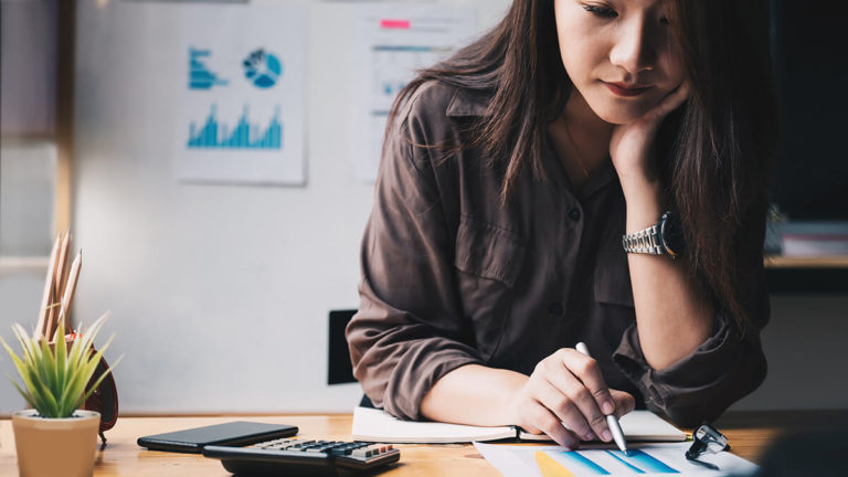 Woman with hand under chin, working on paperwork.
