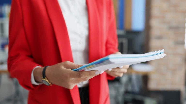 Woman in a red blazer holding a stack of papers.