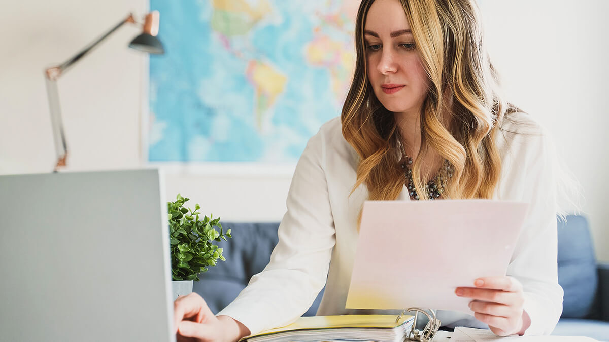 Woman looking at a document and using laptop.