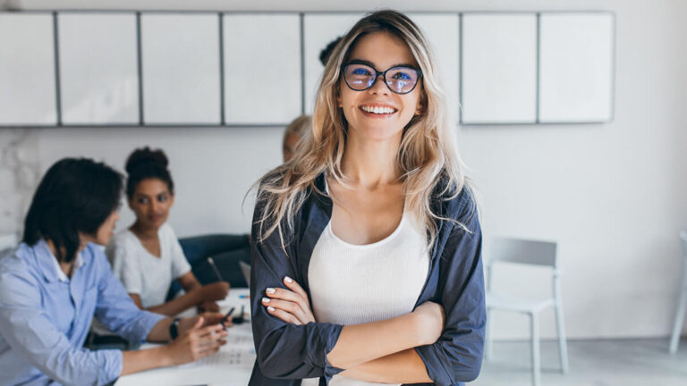 Woman wearing glasses with arms crossed, smiling at camera.