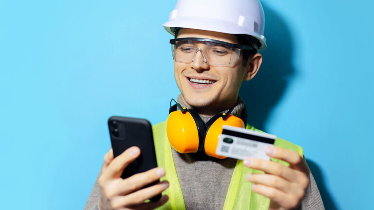 Smiling construction worker entering credit card information into phone.