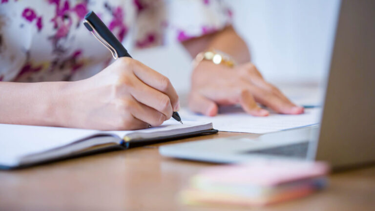 Woman in a flower shirt writing in a notebook.