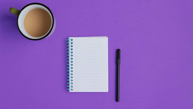 Notebook, pen, and coffee on a purple background.